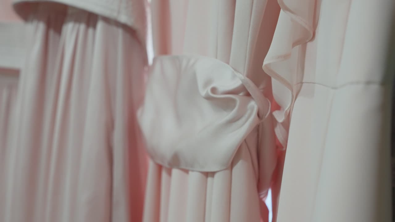 Primo piano dettagliato di eleganti abiti da damigella rosa cipria, con focus su una liscia fascia di raso legata in vita, che mostra le morbide texture del tessuto e lo stile nuziale femminile.