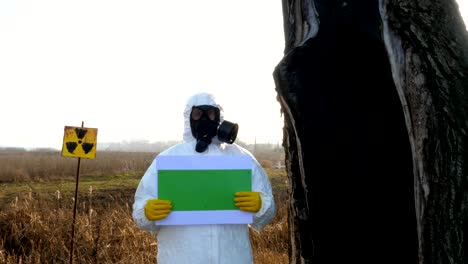 green background, chroma key, a man in a gas mask holds in his hands, a sign of radiation, a burnt tree, a factory with his back.