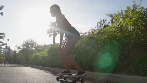 Amidst-palm-trees,-a-young-woman-rides-a-longboard-in-slow-motion,-wearing-shorts-and-sneakers-to-embrace-the-summer-atmosphere