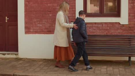 A woman and a boy walking and interacting on a city sidewalk