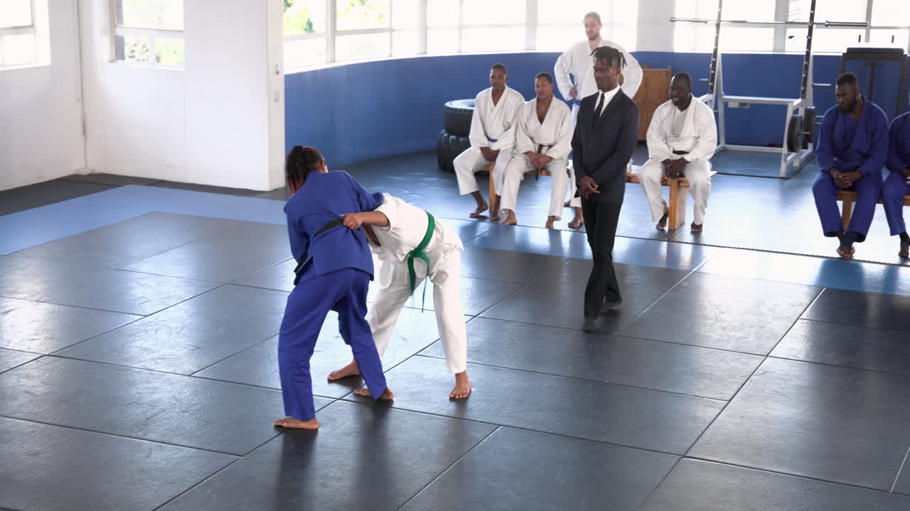 Practicing judo, two athletes sparring on mat while others watch attentively