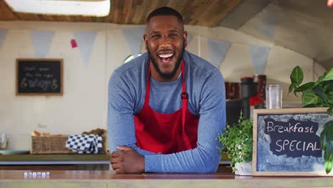 Portrait-of-african-american-man-wearing-apron-smiling-while-standing-in-the-food-truck
