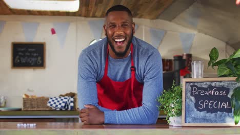 portrait of african american man wearing apron smiling while standing in the food truck