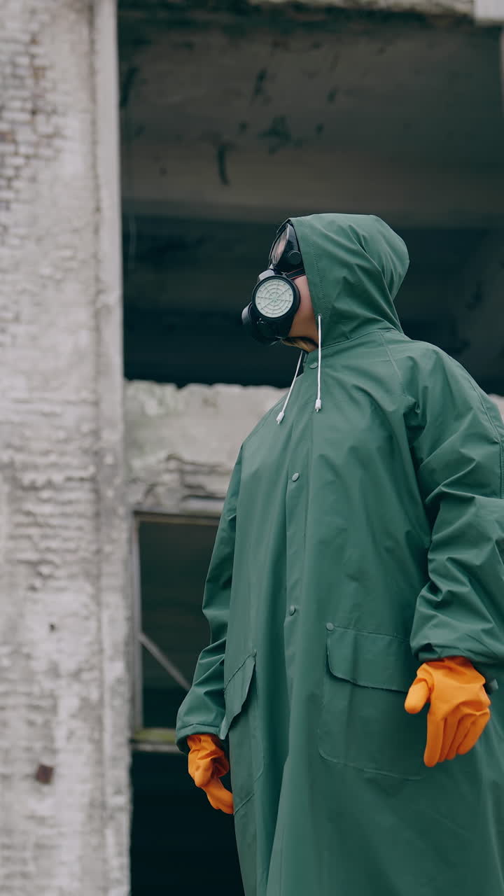 Person in a gas mask and safety suit outdoors. Man wearing respirator and protective uniform standing at post-apocalyptic place. Chemical attack. Vertical video