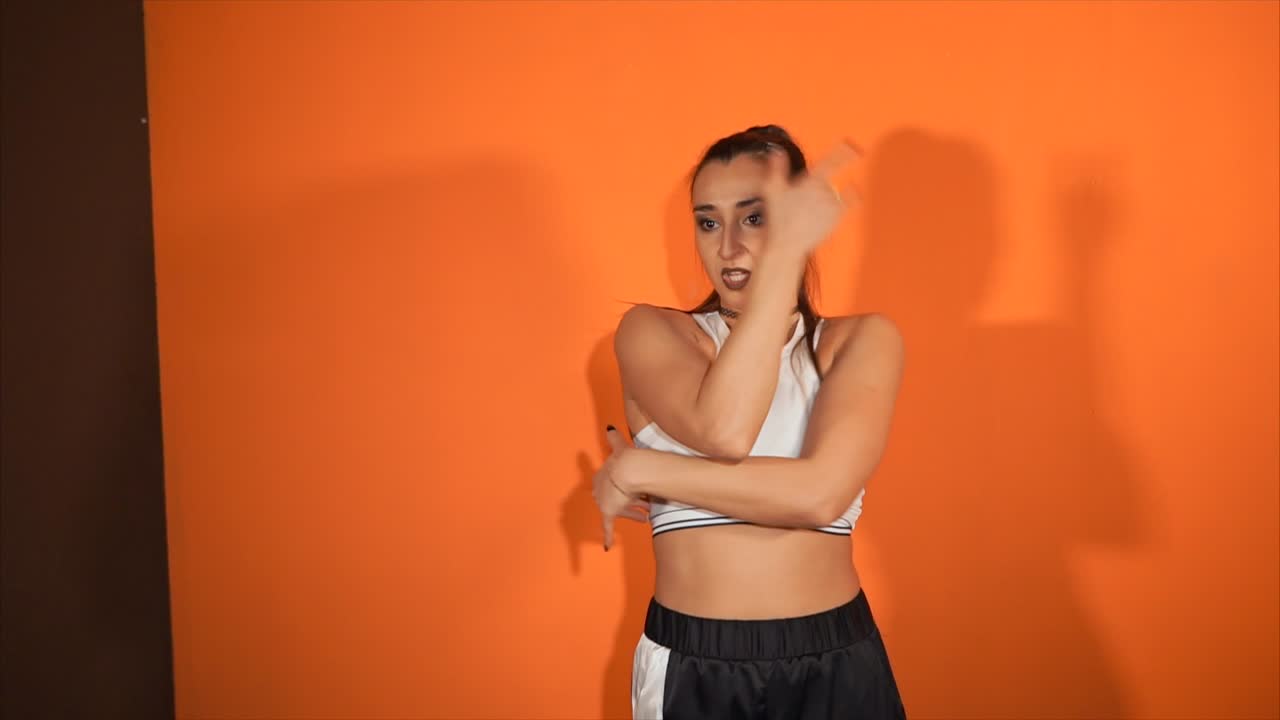 Woman dancing in sporty outfit against orange background