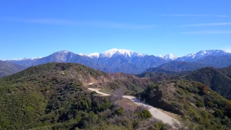 sobrevuelo aéreo de una carretera de montaña sinuosa, dirigiéndose hacia montañas cubiertas de nieve en el fondo