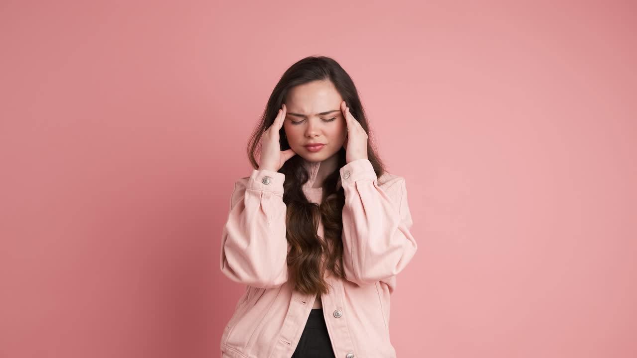 Upset woman suffering from headache in pink studio