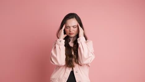 upset woman suffering from headache in pink studio