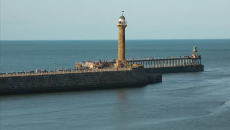 whitby pier evening sunshine with crowds of tourists on the pier and pleasure cruises passing