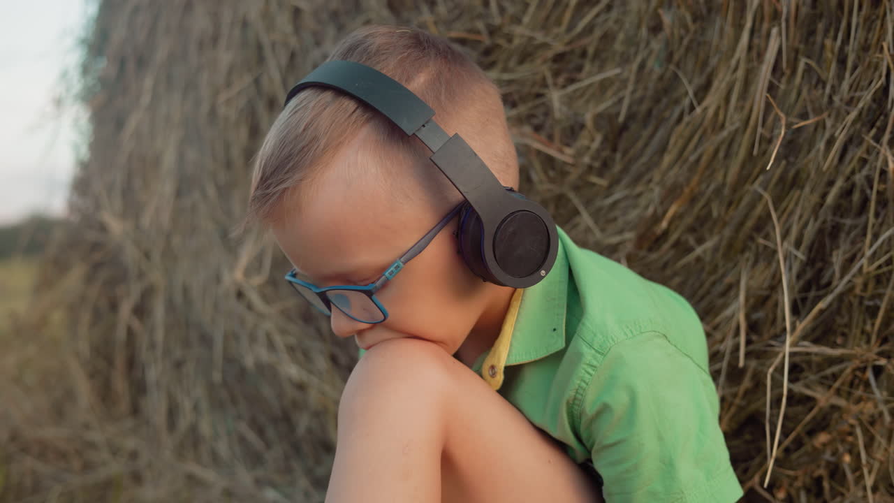 헤드폰과 안경을 쓴 소년은 음악에 깊이 몰입하고 무에 머리를 고, 배경에는 광활한 농장이 펼쳐져 있습니다.