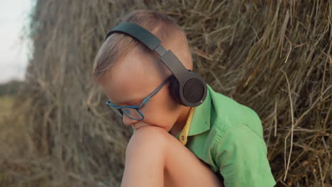 niño con auriculares y gafas profundamente inmerso en la música, apoyando su cabeza en su rodilla, con una vasta tierra de cultivo que se extiende en el fondo