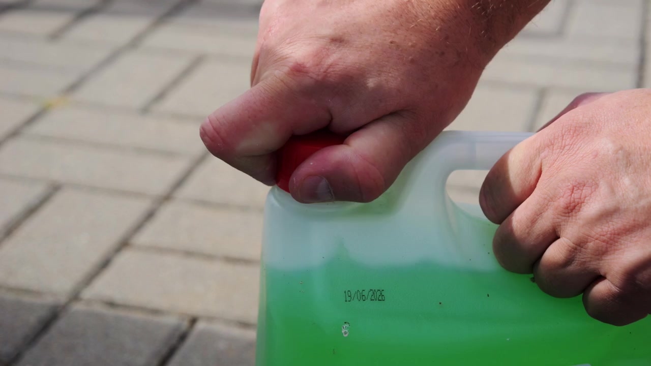 Close view of a driver opening a container of windshield washer fluid before adding it to a vehicle