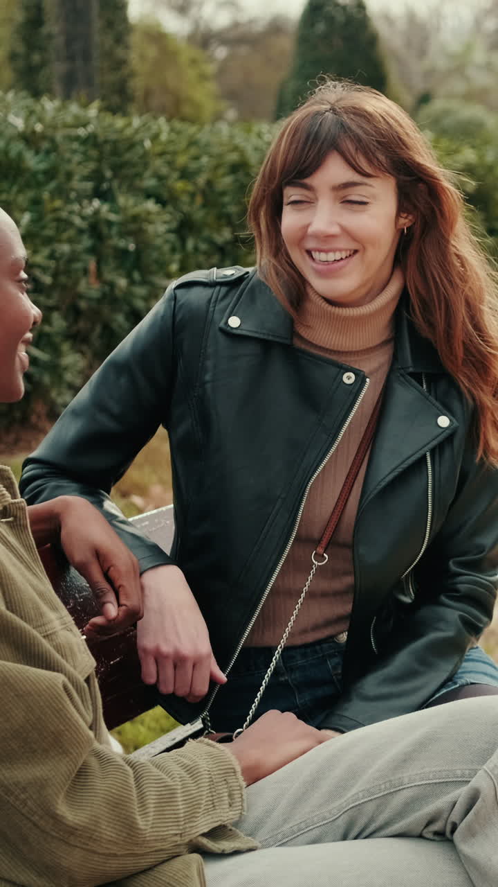 Due giovani donne che parlano e sorridono su una panchina del parco.