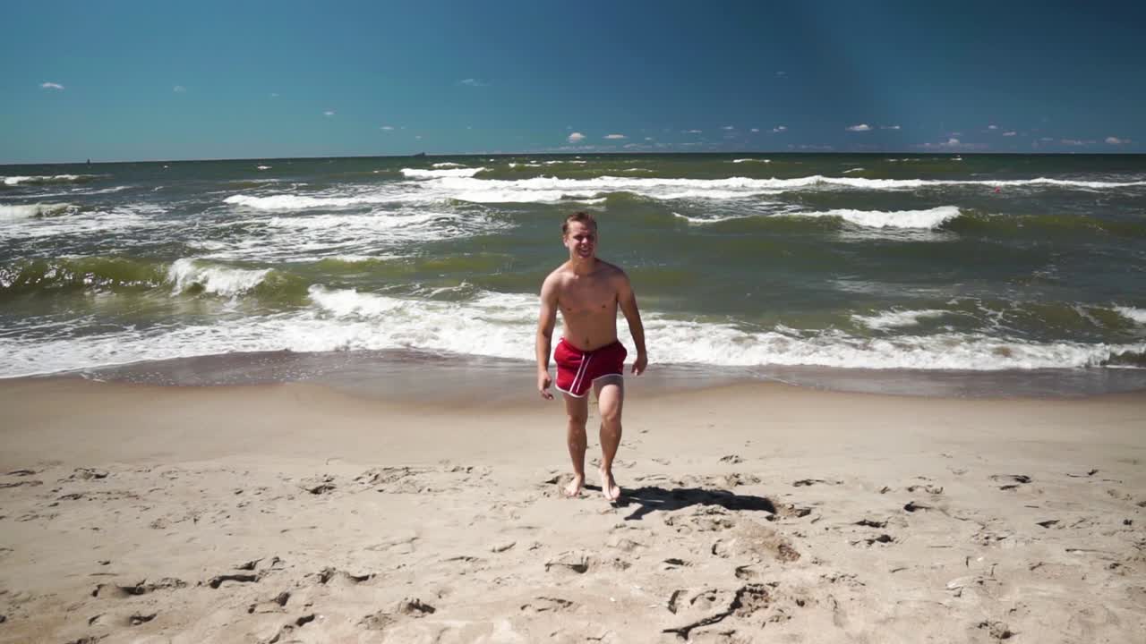 un joven con shorts rojos viene del mar en una playa