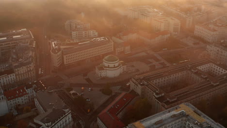 Fly-above-urban-neighbourhood.-Church-or-chapel-with-dome-on-Three-Crosses-Square-in-central-district.-Golden-mist-at-sunrise.-Warsaw,-Poland