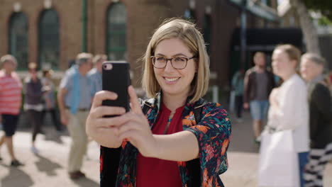 Retrato-De-Una-Mujer-Rubia-De-Moda-Posando-Tomando-Una-Foto-Selfie-Usando-Un-Teléfono-Inteligente-Disfrutando-De-Un-Viaje-Urbano-Soleado