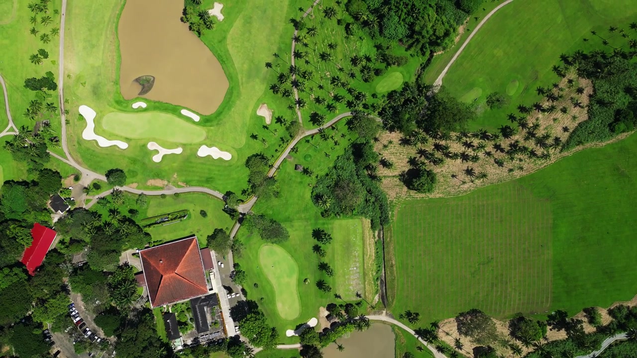 Atmospheric drone footage revealing panoramic views of championship golf landscapes surrounded by mature trees and scenic mountains in Calamba Laguna Philippines.
