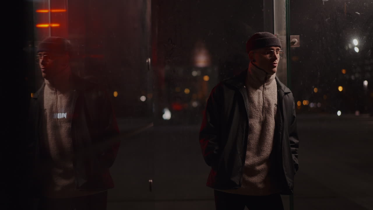 Man in Beanie and Glasses Reflects at Night in an Urban Setting