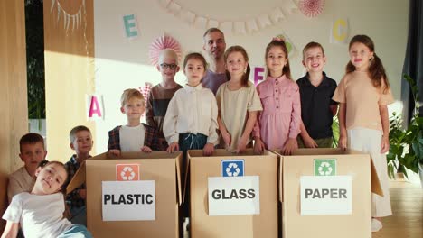 retrato de niños felices junto con su maestro cerca de cajas especiales para clasificar la basura en el clubhouse para preparar a los niños para la escuela. retrato de un grupo de niños aprendiendo a clasificar la basura