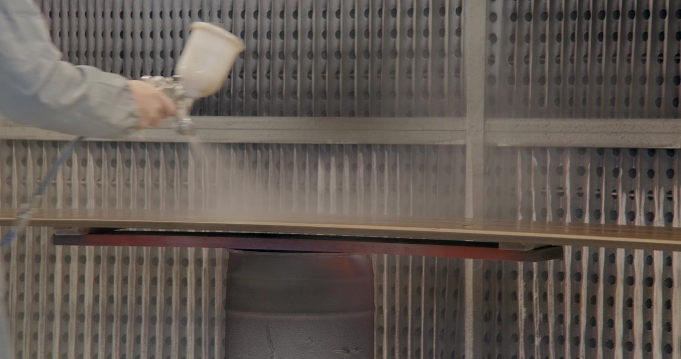 Closeup on artisan spray painting a wooden plank