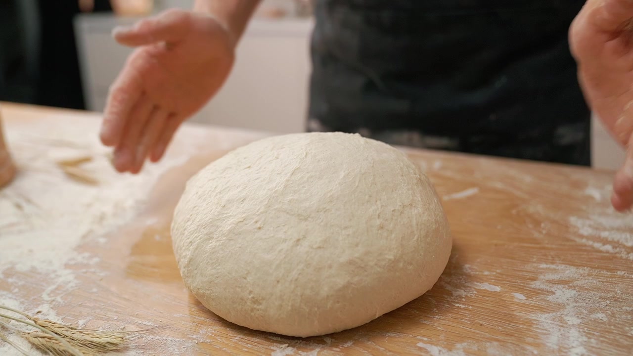 Primo piano di mani che posizionano impasto crudo su un tavolo di legno infarinato