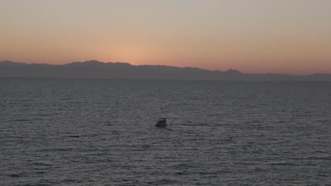 Small-sailing-boat-travelling-across-Mediterranean-sea-towards-glowing-orange-sunset-skyline