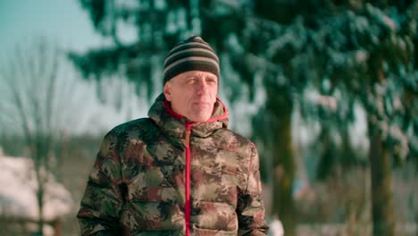 a person wearing a camouflage jacket walks on camera a forest pathway covered in snow on a winter day