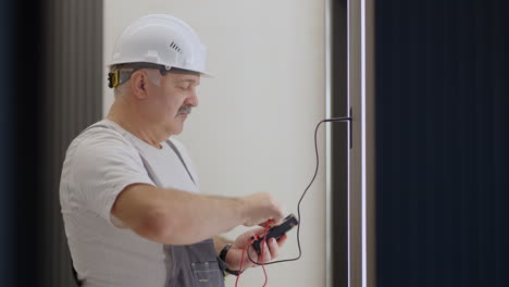 elderly electrician checks the operation of the wall control unit of lamps with the system of a modern house after installation and repair