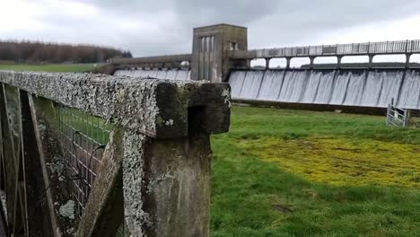 cefni dam slow motion dolly across wooden gate to reveal concrete wall overflow pouring from llangefni reservoir