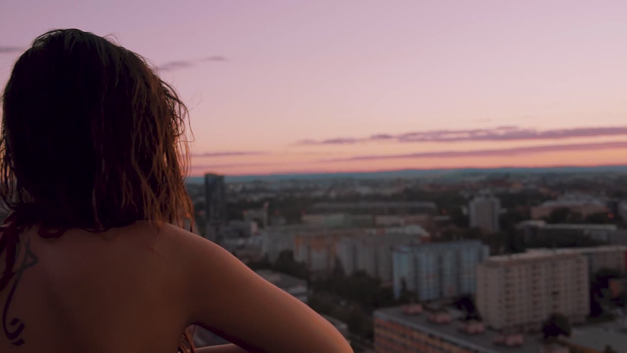 Beautiful sexy young woman enjoying the majestic view of city from the high elevated balcony of hotel room. View from back