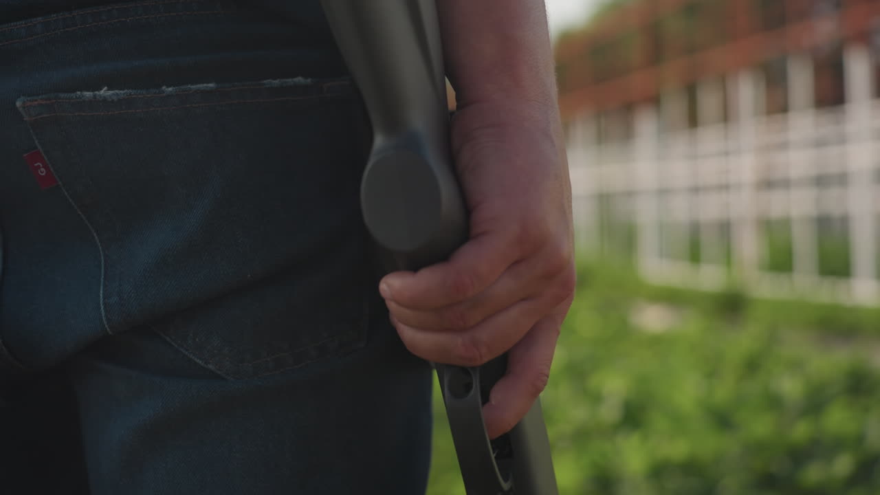 Closeup farmer in jeans holds rifle on farm during pest control, hand gripping stock near trigger, metal frame structure and garden in background