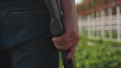 closeup farmer in jeans holds rifle on farm during pest control, hand gripping stock near trigger, metal frame structure and garden in background