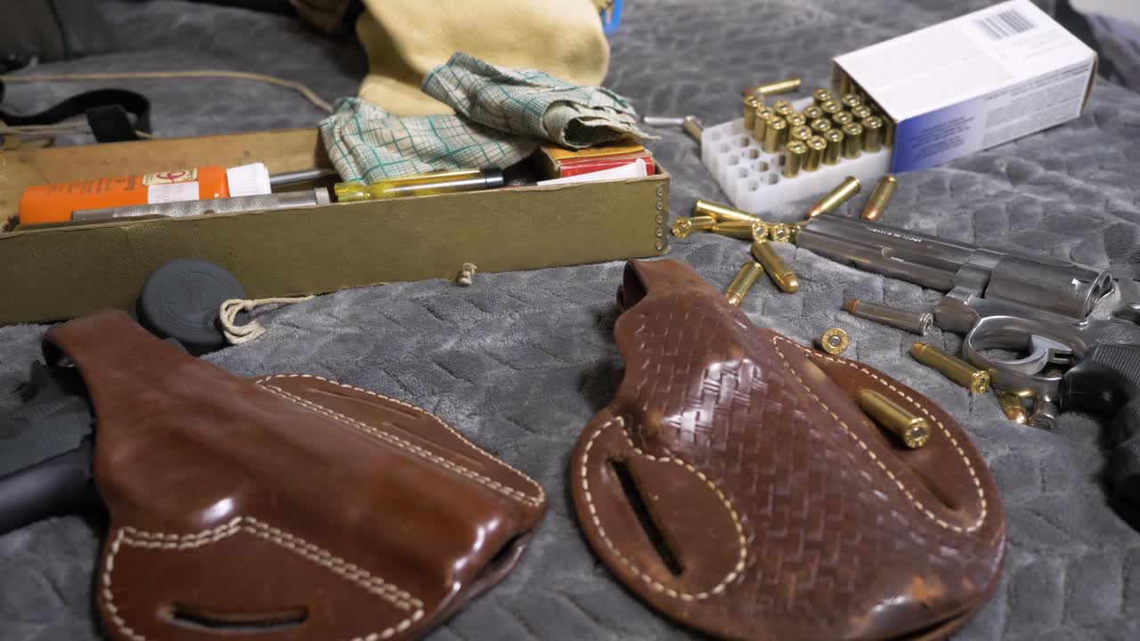 60p-Zeitlupe: Langsamer Schwenk nach links über Revolver und Pistolen in Holstern mit herumliegender Munition