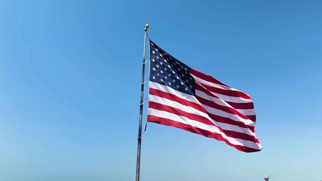 Filmisk stockoptagelse af det amerikanske flag, der vajer stolt i den stærke vind under skarpt sollys. B-roll af høj kvalitet til patriotiske og kommercielle projekter.