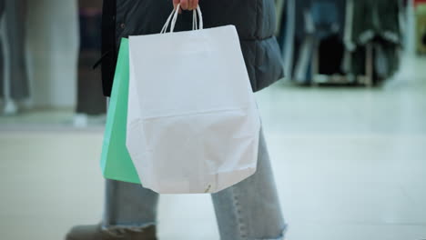 side view of lady walking past retail space in well-lit mall mannequin dressed in clothing and garments arranged on racks visible, partial view of another shopper seen through glass display