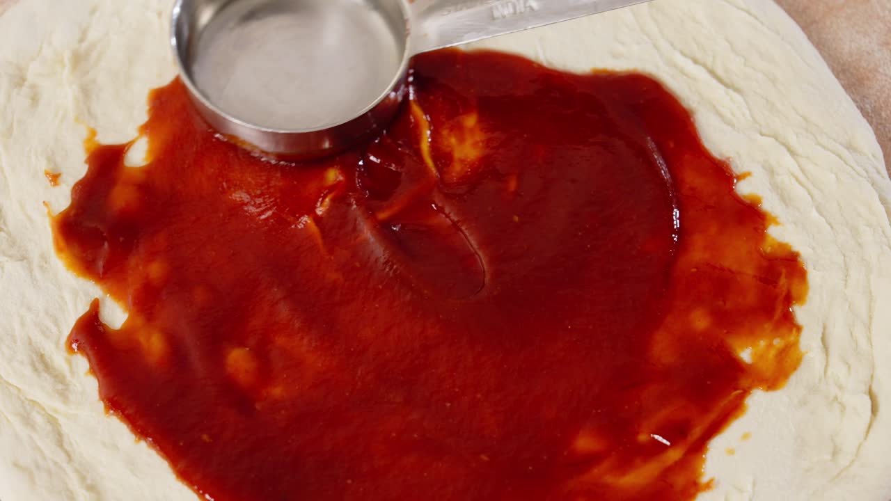 Spreading tomato sauce over a pizza top view