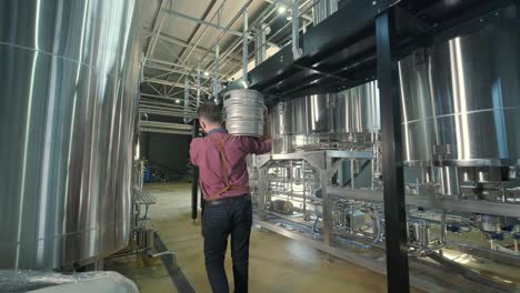 un joven cervecero con un delantal de cuero lleva un barril de cerveza artesanal en una cervecería moderna