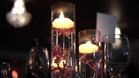 wedding reception table centerpiece with flowers and floating candles and with a chandelier in the background