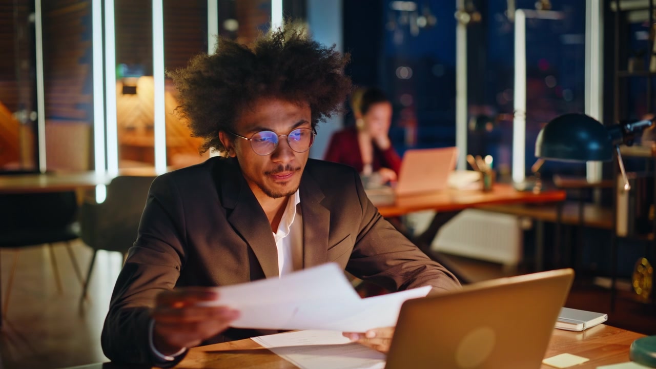Focused specialist reading documents night office. Businessman checking papers.