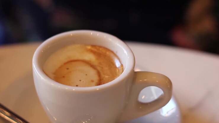 Primo piano di mano che mescola un espresso in una tazza bianca