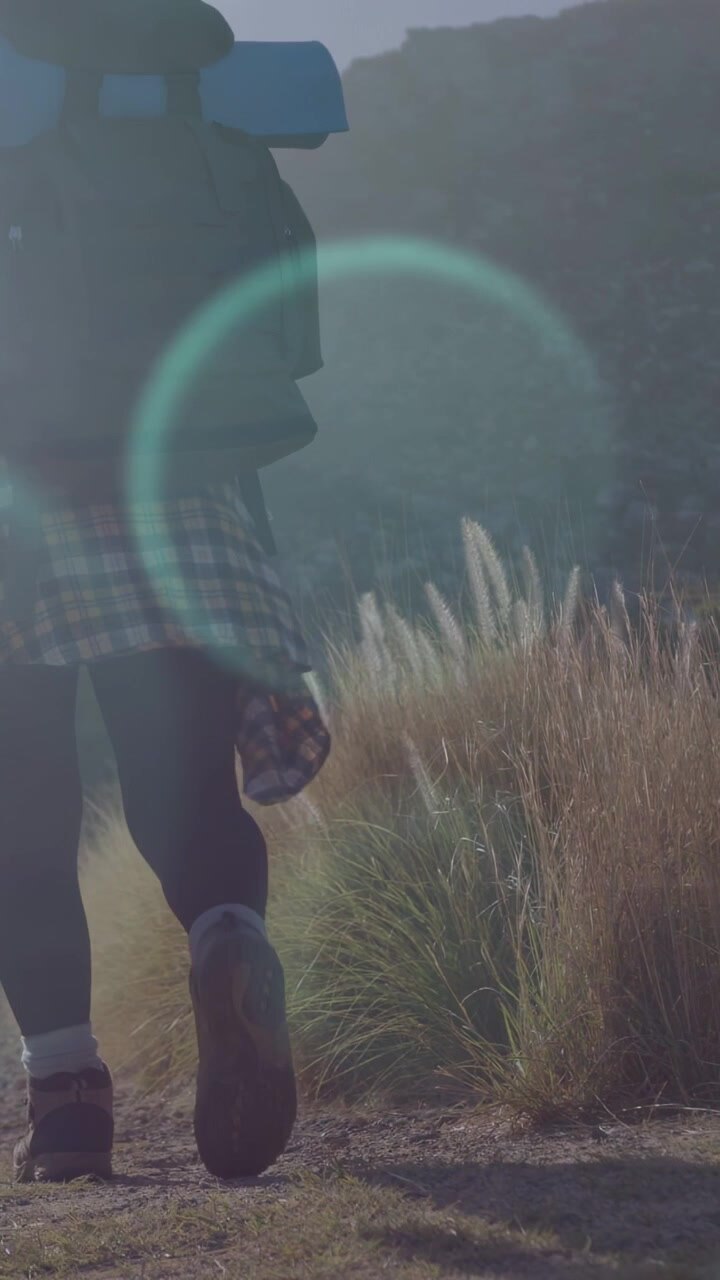 Vertical video: Woman hiker backpacking boot starting tracking, walking toward ridge lens flare