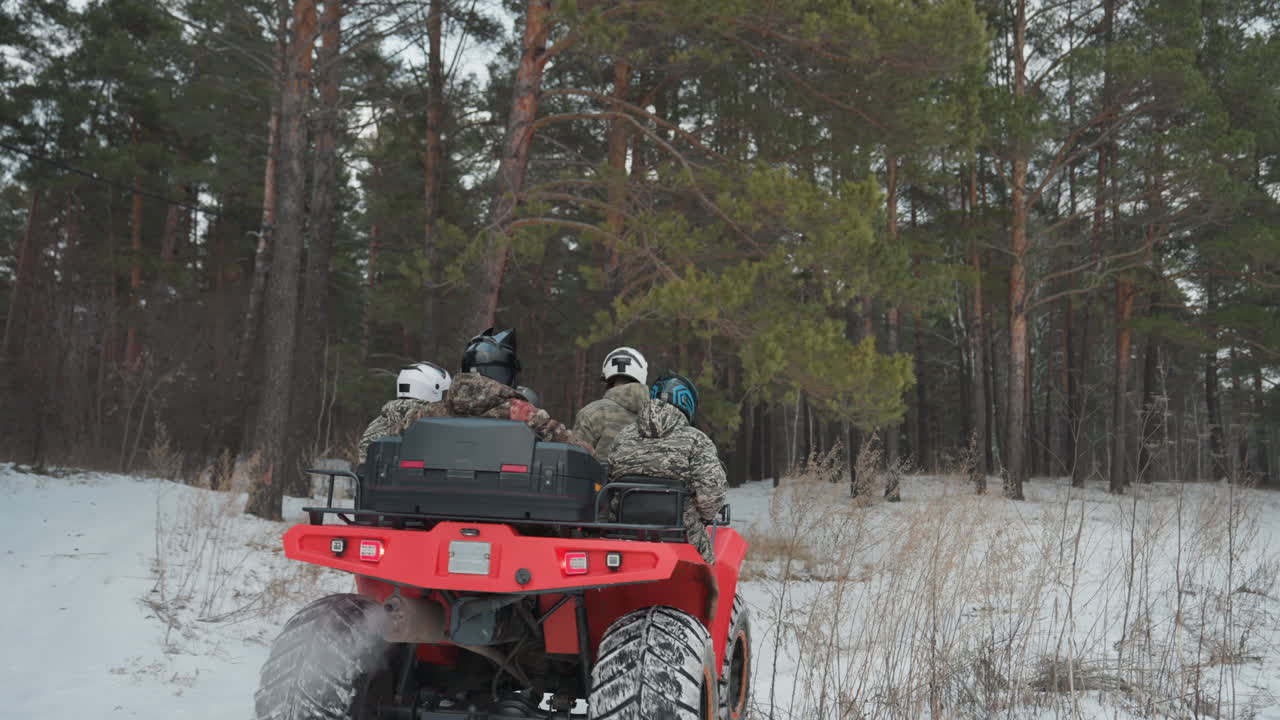 Vista posteriore di un ATV rosso che si addentra nel bosco con piloti caucasici, spruzzi di neve e fumo di scarico, stretto sentiero di pini, giacche mimetiche e caschi, movimento dinamico e segni di derapata, sensazione di inseguimento cinematografico.