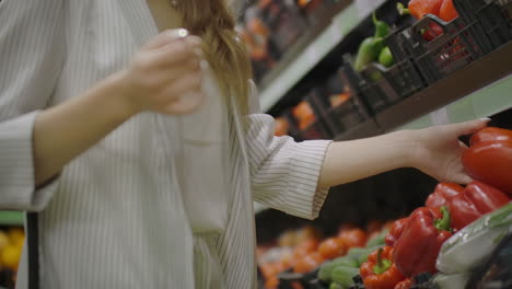 woman buying red pepper in supermarket. female hand choosing organic vegetables in grocery store. zero waste shopping and healthy lifestyle concept. slow motion