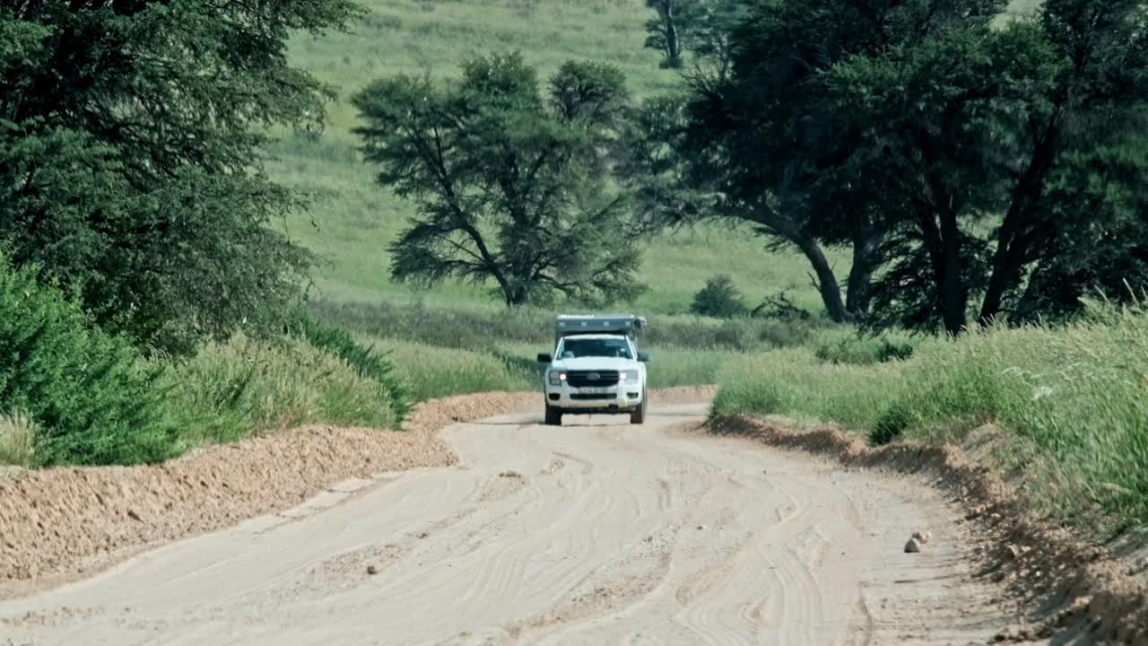 4x4 off road safari vehicle with a roof tent driving in the Kalahari national park in South Africa, on a dirt road, after he rain, with lush trees and grass in the background