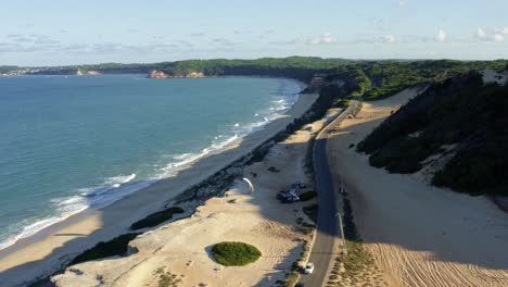 Extrem-Weit-Nach-Oben-Geneigte-Luftdrohnenaufnahme-Der-Berühmten-Tropischen-Küste-Im-Nordosten-Brasiliens-Mit-Der-Touristenstadt-Pipa-Im-Hintergrund-Und-Von-Klippen-Umgebenen-Stränden-In-Rio-Grande-Do-Norte