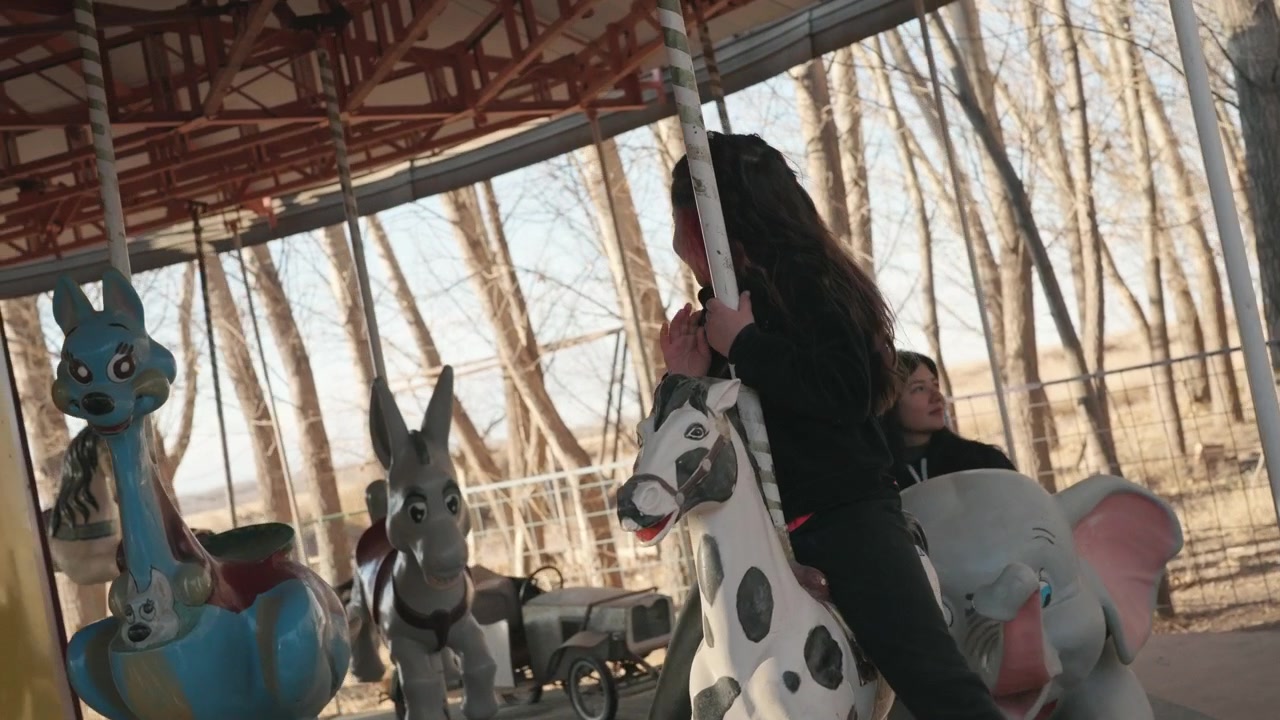 Jovem garota anda em carrossel em cenário de floresta ao ar livre, tomada cinematográfica de estilo de vida destacando a alegria infantil, movimento lúdico e atmosfera nostálgica de parque de diversões durante a recreação