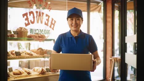 a cheerful employee in a blue uniform carrying a box out of a bakery, showcasing a welcoming atmosphere filled with delicious pastries and the aroma of fresh baked goods