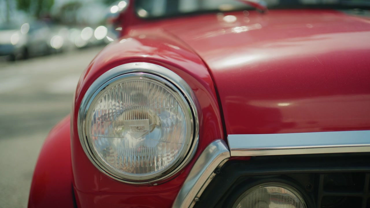 Detailliertes kinoreifes Filmmaterial eines klassischen roten Oldtimer-Automobils von außen, mit weichgezeichnetem Hintergrund und polierten Retro-Designelementen in sonniger Außenumgebung