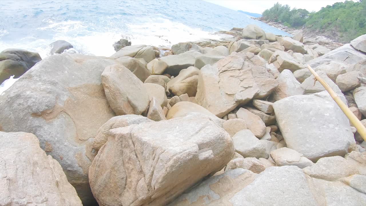 FPV Shot of a Man exploring and advancing in a rocky beach terrain in Phuket, Thailand.