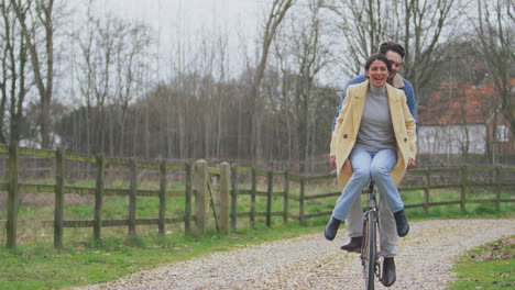 Amorosa-Pareja-Transgénero-Con-Una-Mujer-Montada-En-El-Manillar-De-Una-Bicicleta-En-El-Campo-De-Otoño-O-Invierno